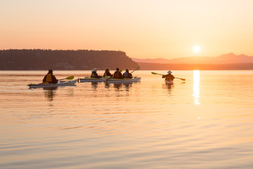 Group of people men and women in kayaks sea kayaking. Active outdoor adventure water sports enjoying beautiful nature at sunrise.