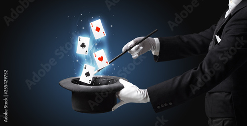 Magician with white gloves conjuring playing cards from a cylinder with magic wand