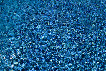 Swimming pool bottom caustics ripple and flow with waves background. Surface of blue swimming pool, background of water in swimming pool. Clear light blue pool water ripples with sun reflections.