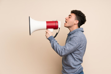 Young man over isolated wall shouting through a megaphone