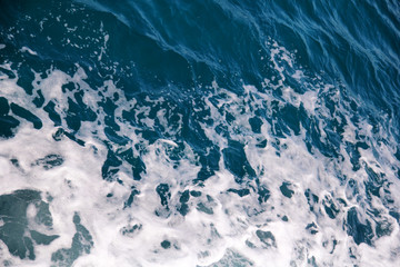 Turbulence made by foam of sea water from a high-speed yacht on surface of sea. Blue sea waves with lot of sea foam. Surface of sea with waves, splash, foam and bubbles, blue background and wallpaper.