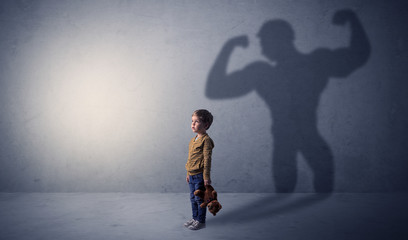 Little waggish boy in an empty room with musclemen shadow behind
