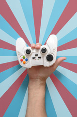 Hand holds a white joystick console like sign of the horns. Colorful background.