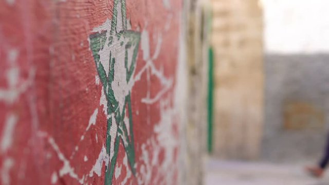Flag of Morocco with a Green star flag of Morocco on street wall in Essaouira Medina. Local people are passing by on a blured background street