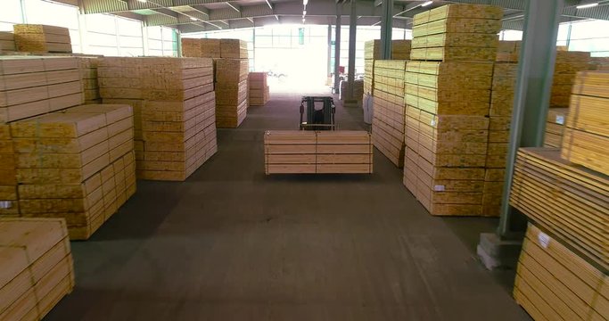 A forklift carries a wooden beam through the sawmill's warehouse. Modern warehouse sawmill. A large warehouse of timber materials. Neatly stacked wooden bar in a sawmill warehouse