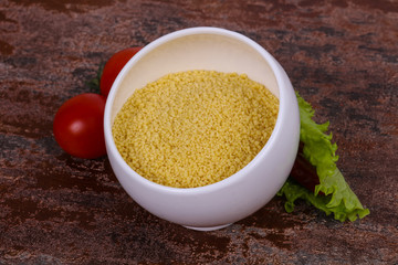 Raw couscous in the bowl served salad leaves, tomato and pepper