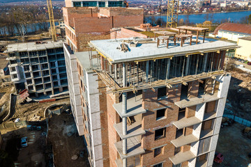 Apartment or office tall building under construction, top view. Brick walls, scaffolding and concrete support pillars. Tower crane on bright blue sky copy space background. Drone aerial photography.