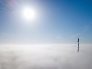 Obraz premium Aerial top view of foggy cloudy landscape with radio or TV antenna top on blue sky copy space background and mountain ridge on horizon.