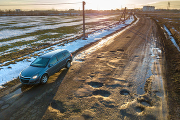 Aerial view of car moving along muddy rural road in bad condition on sunny spring or winter day.
