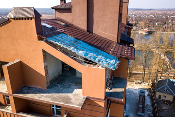 Aerial top view of unfinished tall apartment building, annex room under construction, high chimneys and plastic windows on tiled roof.