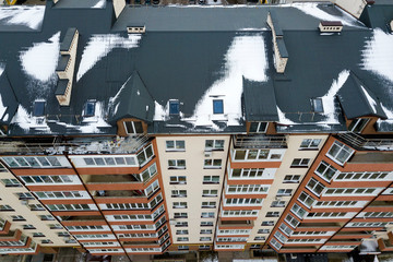 Fototapeta premium Aerial winter top view of tall apartment building, brick chimneys, tiled roof. Urban infrastructure, view from above.