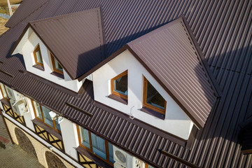 Close-up aerial view of building attic rooms exterior on metal shingle roof, stucco walls and plastic windows. © bilanol