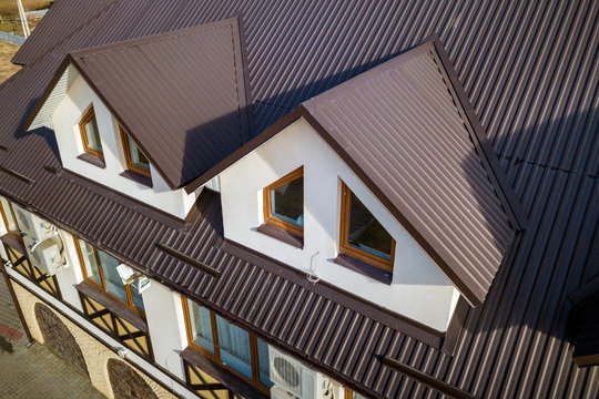 Close-up aerial view of building attic rooms exterior on metal shingle roof, stucco walls and plastic windows.