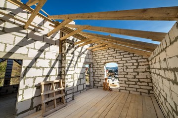 House interior under construction and renovation. Energy saving walls of hollow foam insulation blocks and bricks, ceiling beams and roof frame.