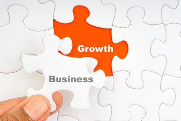 Fototapeta premium Hand holding piece of jigsaw puzzle with word BUSINESS GROWTH. Selective focus