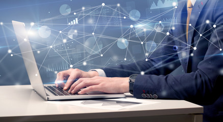 Businessman typing on laptop with linked reports charts grapghs around
