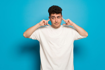 Fototapeta na wymiar Young man over blue background covering both ears with hands