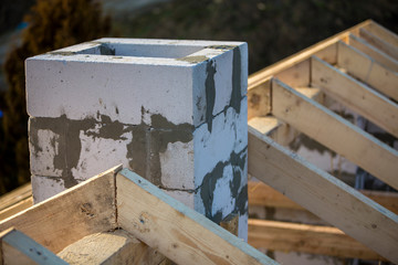 Close-up detail of roof frame of rough wooden lumber beams and chimney made of foam insulation blocks on blurred green background. Building, roofing, construction and renovation concept.