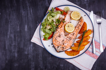 Fried salmon with lemon, potatoes, salad and spices on a black wooden table