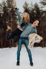 Obraz premium happy cheerful smiling man with girl and dog on his hands. couple of young people in denim suits in snowy forest in winter with red dog border collie . place for text. winter holiday