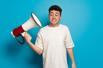 Young man over blue background taking a megaphone that makes a lot of noise
