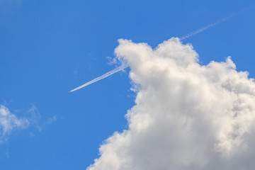 Jet aircraft with condensation trail on a blue sky with white clouds in sunny day