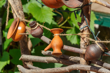 Handmade small clay jugs hanging on a rope on the braided fence
