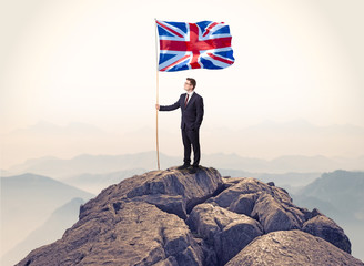Obraz premium Successful businessman on the top of a mountain holding victory flag 