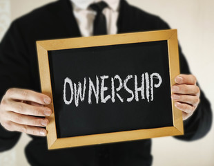 male businessman in a suit with tie holds in his hand a sign with the inscription OWNERSHIP