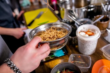 Cook takes boiled noodles in a colander. Master class in the kitchen. The process of cooking. Step by step. Tutorial. Close-up