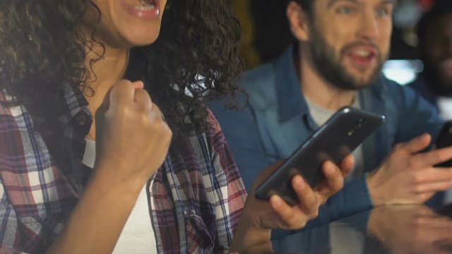 Friends with smartphones cheering for sports team victory in bar, betting online