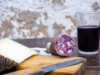Iberian pork sausages on an old wooden board with a wedge of sheep cheese, an antique knife and a glass of red spanish wine