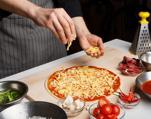 Man sprinkling pizza with cheese at kitchen