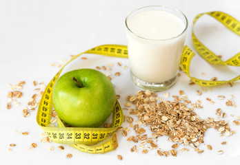 Green apple, oat flakes, yogurt and yellow measuring tape on a white table