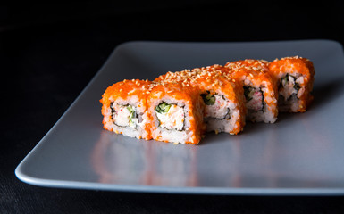 Sushi California Roll with crab meat, cucumber, masago on a gray plate, black background, side view
