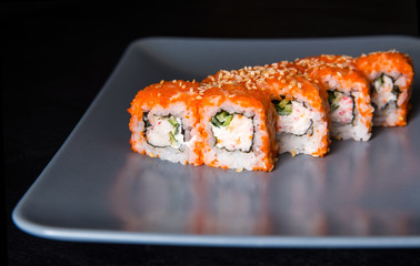 Sushi California Roll with crab meat, cucumber, masago on a gray plate, black background, side view