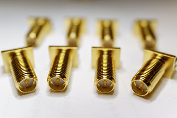Close-up of scattered gold plated SMA male connectors electronics components in partial focus on white background