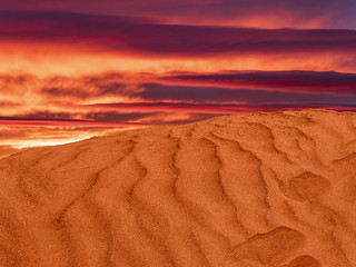red sand hill in the desert. ripples in the sand with the purple clouds