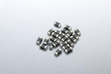 Abstract close-up of grey scattered 0402 SMT surface mount chip ferrite bead power electronics components on white background in random pattern