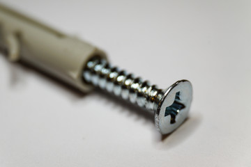 Macro close-up of chrome screw thread and beige dowel on white background in partial focus