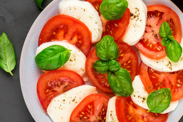 close up of italian caprese salad with sliced tomatoes, mozzarella cheese, basil, olive oil, pepper in a plate