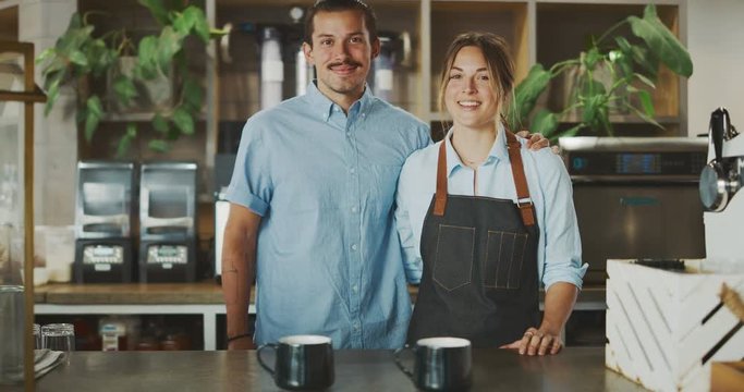 Portrait of two smiling attractive baristas in coffee shop, young trendy baristas, artisan coffee shop lifestyle