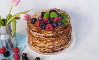 Pancakes on a saucer with raspberries and blackberries and a piece of butter. Spring bouquet of tulips. Lots of pancakes stacked. Thin pancakes with crispy crust. Carnival. Copy space.