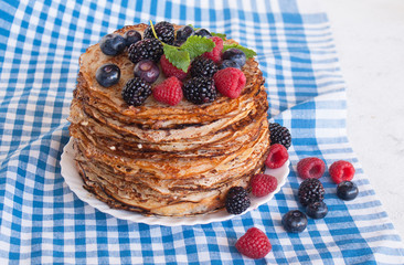 Pancakes on a platter with raspberries, blueberries and blackberries on a kitchen towel. Lots of pancakes stacked. Thin pancakes with crispy crust. Carnival.