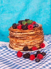 Pancakes on a platter with raspberries, blueberries and blackberries on a kitchen towel. Lots of pancakes stacked. Thin pancakes with crispy crust. Carnival.