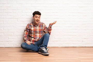Young man sitting on the floor holding copyspace imaginary on the palm to insert an ad