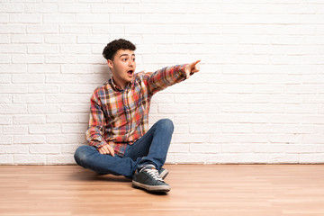 Young man sitting on the floor pointing away