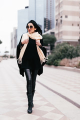 Outdoors fashion portrait of stunning trendy woman posing on the street. Smiling and walking on the city. Going shopping. Wearing stylish white fitted coat, round rim sunglasses. Waiting for. Close up