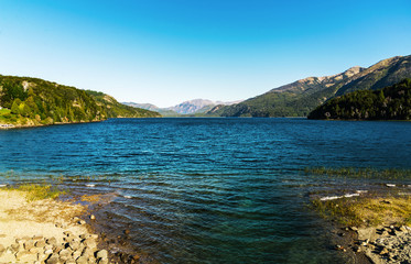 Colorful nature scenic photo of transparent aquamarine blue water surface of a lake with forest and Andes mountains in Patagonia, Argentina