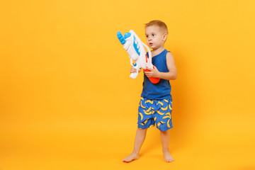 Kid boy 3-4 years old in blue beach summer clothes hold toy water gun isolated on bright yellow orange wall background children studio portrait. People childhood lifestyle concept. Mock up copy space.